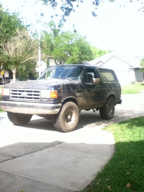 1988 Ford Bronco - This black Ford Bronco is parked on a concrete driveway with grass and trees in the background.
