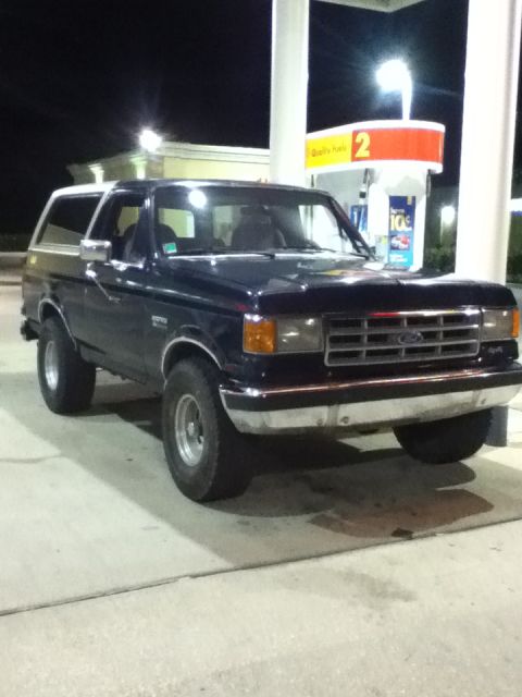 1988 Ford Bronco - Dark blue 1988 Ford Bronco at a gas station pump under artificial lighting.