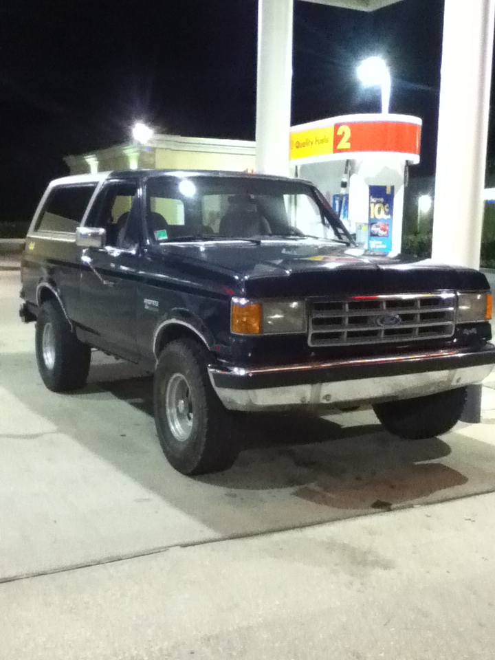 1988 Ford Bronco parked at a gas station pump at night