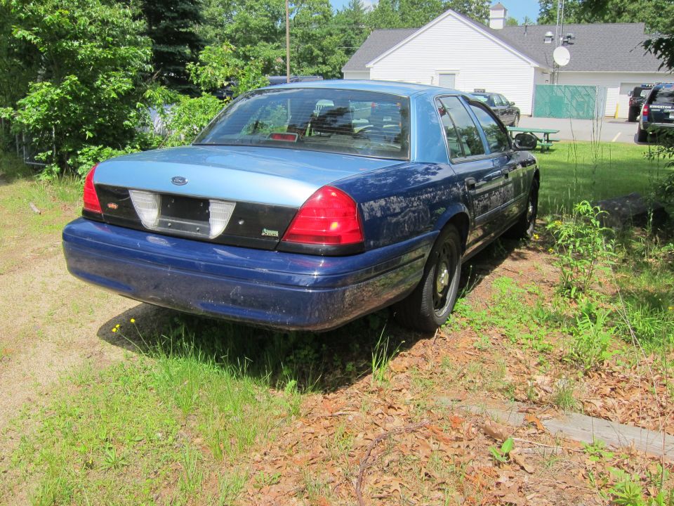 Blue Ford Crown Victoria parked on grass, rear view. Two-tone paint on the trunk and roof