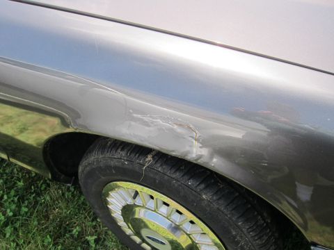 2001 Ford Crown Victoria - Damage is visible on the front fender of a gray car, just above the wheel.