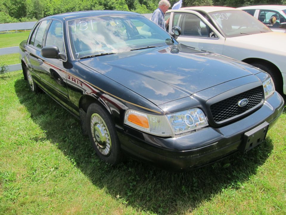 Black 2001 Ford Crown Victoria with 'FIRE' text on the side, parked on grass next to another car