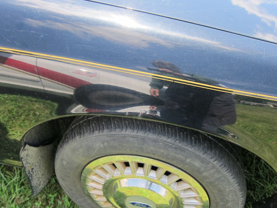 Black car fender with gold pinstripes, dent, and chrome wheel. Tire is visible