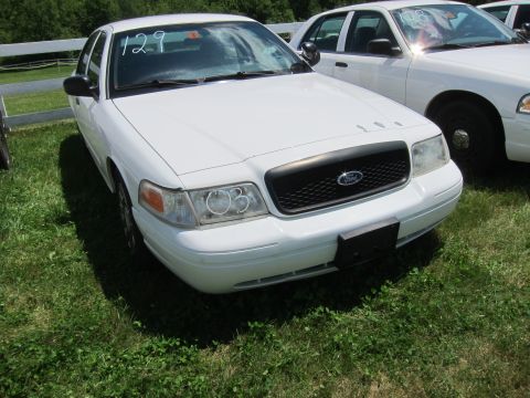 2001 Ford Crown Victoria - A white Ford Crown Victoria is parked on a grassy area with another vehicle visible behind it.