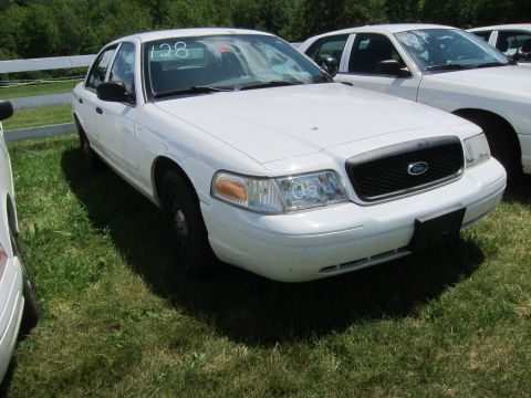 2001 Ford Crown Victoria - A white 2001 Ford Crown Victoria is parked on a grassy lot with other vehicles, displaying the number 128 on its windshield.