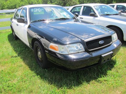 2001 Ford Crown Victoria - Two Ford Crown Victoria police cars parked on grass, one black and white, the other white.