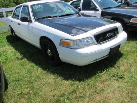 2001 Ford Crown Victoria - A white Ford Crown Victoria with a black hood and steel wheels is parked on grass. The number 06 is visible on the headlight.