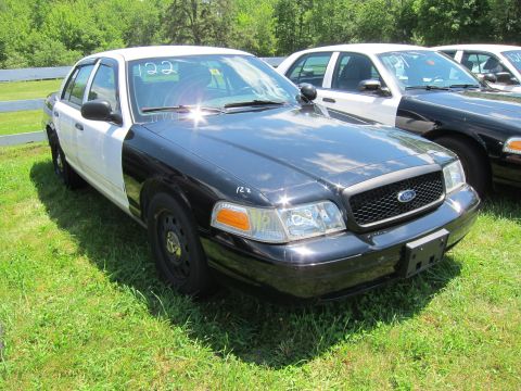 2001 Ford Crown Victoria - Two-tone police car with a light bar on the roof is parked outdoors with other vehicles.