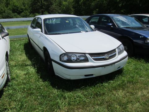 2001 Ford Crown Victoria - A white sedan is parked on grass next to another vehicle, with a white fence in the background.