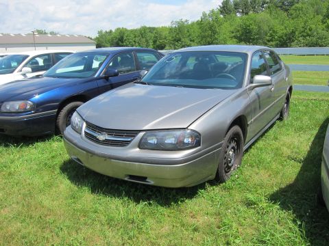 2001 Ford Crown Victoria - A gray Chevrolet Impala is parked on a grassy lot next to other vehicles. The grille has a tag with '05' on it.