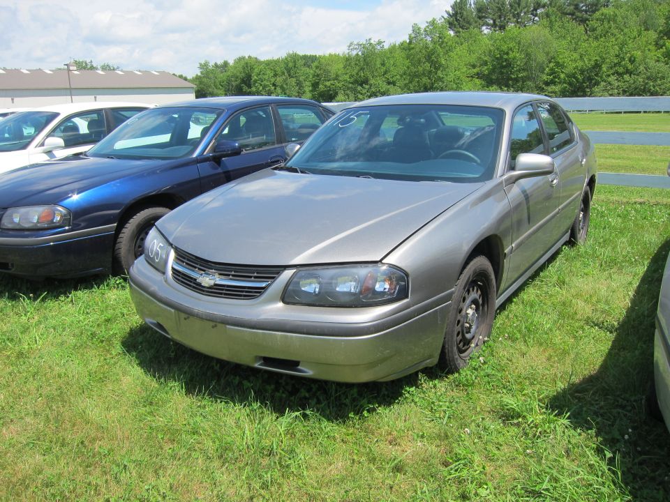 Gray Chevrolet Impala parked on grass next to a blue car. A tag with '05' is on the grille