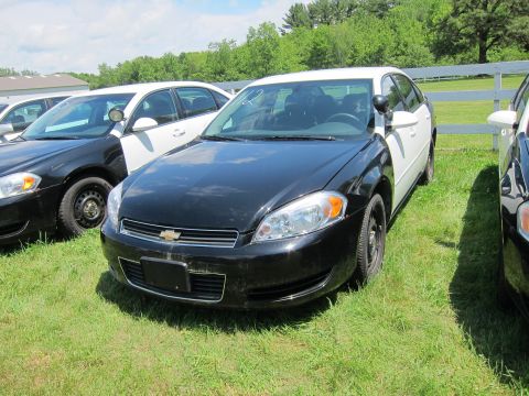 2001 Ford Crown Victoria - Several police sedans are parked in a grassy area under a partly cloudy sky.