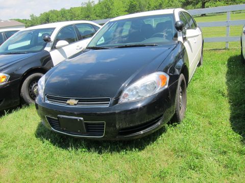 2001 Ford Crown Victoria - Two-tone police cars are parked on a grassy area with a white fence in the background.