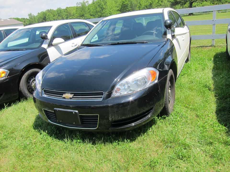 Front view of a black and white police car, possibly a Chevrolet Impala, parked on grass next to another police car