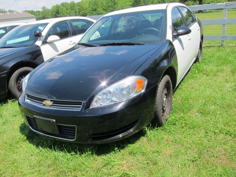 2001 Ford Crown Victoria - A black and white police car is parked on a grassy field next to another similar vehicle.
