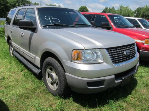 2001 Ford Crown Victoria - Silver SUV parked on grass with '03' written on the headlight. Another red vehicle is parked next to it.