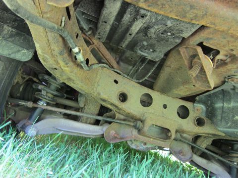 2001 Ford Crown Victoria - The heavily rusted undercarriage of a vehicle is visible, with focus on the frame and suspension components.