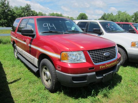 2001 Ford Crown Victoria - A red Ford Expedition with 'Fire Department' text on the bumper is parked on grass next to other vehicles.