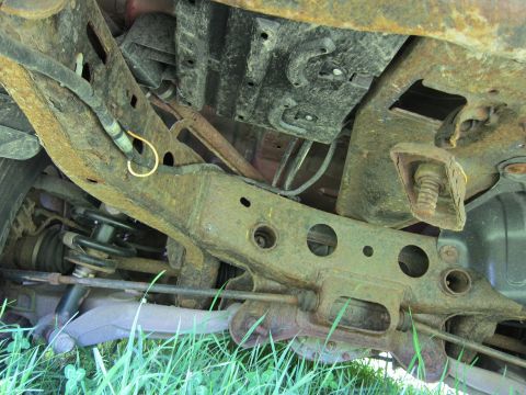 2001 Ford Crown Victoria - The heavily rusted undercarriage of a vehicle is visible, with grass in the foreground.