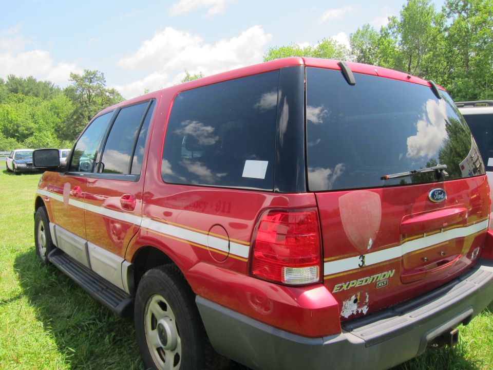 Red Ford Expedition SUV rear view, with white and yellow stripes, "EXPEDITION" badge visible, some damage on bumper
