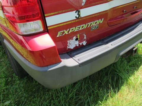 2001 Ford Crown Victoria - The rear of a red SUV shows 'EXPEDITION XLT' badging and a damaged section on the tailgate.