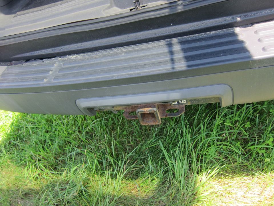 Rear bumper and rusted trailer hitch on a vehicle, with grass in the foreground