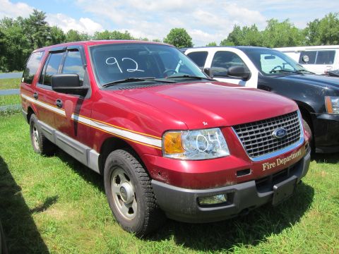 2001 Ford Crown Victoria - This red Ford Expedition SUV has 'Fire Department' text on the front grille. It is parked on grass next to another vehicle.
