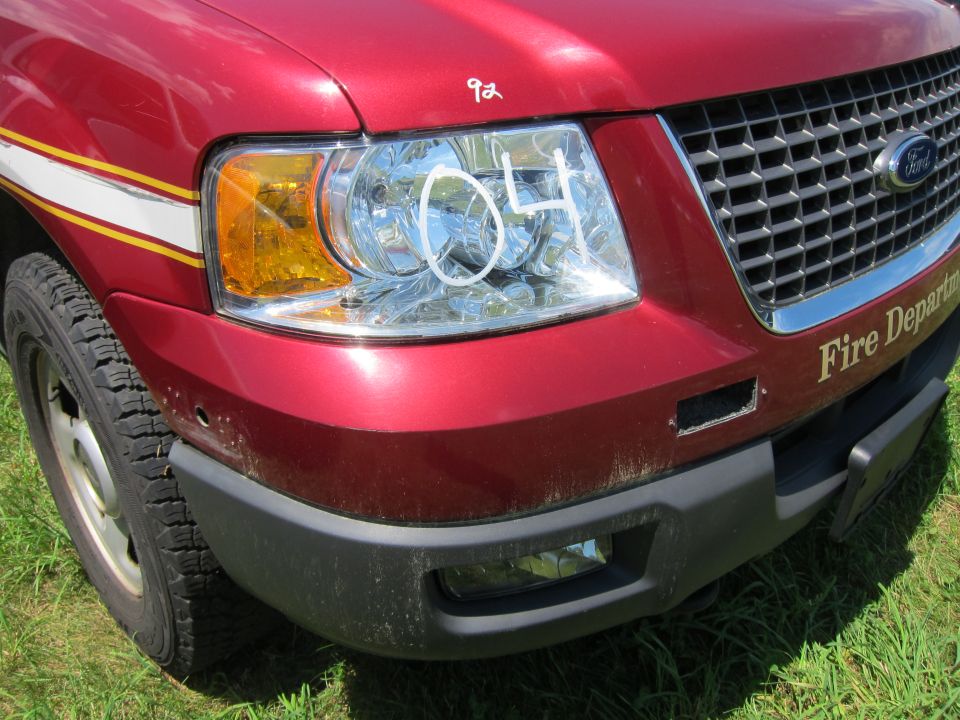 Red Ford SUV front corner with yellow turn signal, chrome grille, and 'Fire Department' text