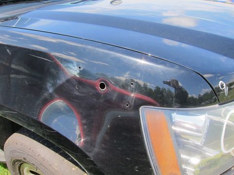 2001 Ford Crown Victoria - Close-up of a damaged black car fender showing dents and bullet holes.