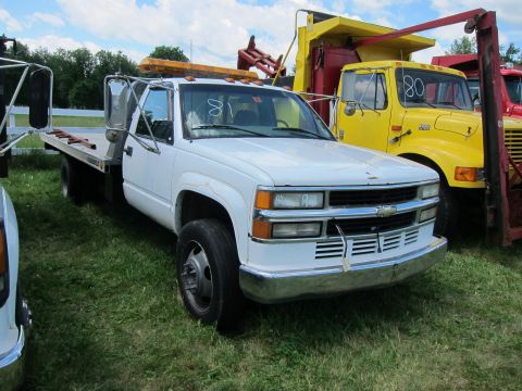 2001 Ford Crown Victoria - A white flatbed truck is parked on grass, with a yellow truck visible behind it.