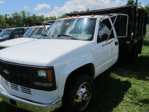 2001 Ford Crown Victoria - A white dump truck is parked in a grassy lot next to another truck under a partly cloudy sky.