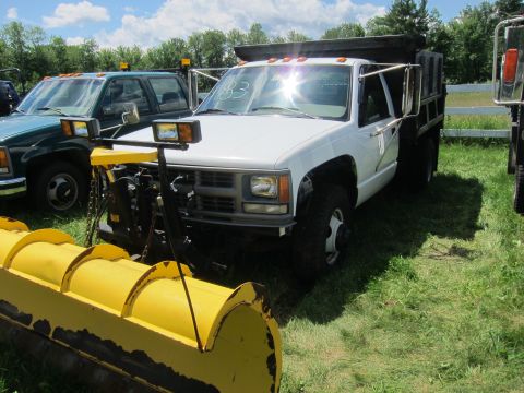 2001 Ford Crown Victoria - White dump truck with a yellow snow plow is parked on grass next to another truck.