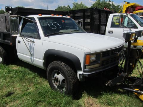 2001 Ford Crown Victoria - A white dump truck with a plow attachment is parked on grass next to another white truck.