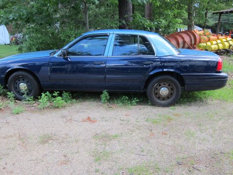 2001 Ford Crown Victoria - A blue Ford Crown Victoria is parked outdoors next to some overgrown grass and trees.