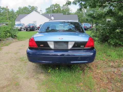 2001 Ford Crown Victoria - Rear view of a blue 2001 Ford Crown Victoria, with two other police vehicles parked in the background.