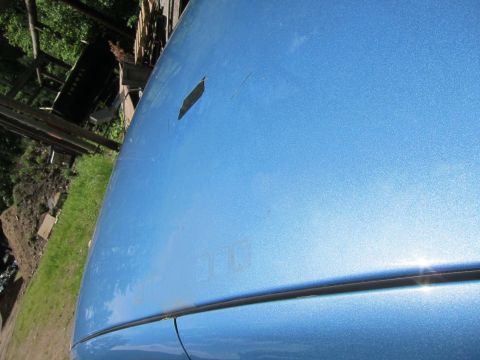 2001 Ford Crown Victoria - Close-up of a blue car's hood showing minor damage and a faint outline of a previous decal.