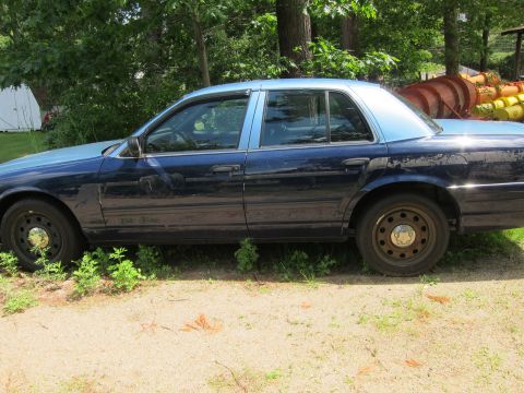2001 Ford Crown Victoria - A dark blue and light blue sedan is parked outdoors on a dirt and grass area.