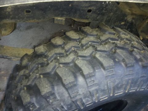 1986 Ford Bronco - This image shows a close-up view of a off-road tire and the vehicle's undercarriage components.