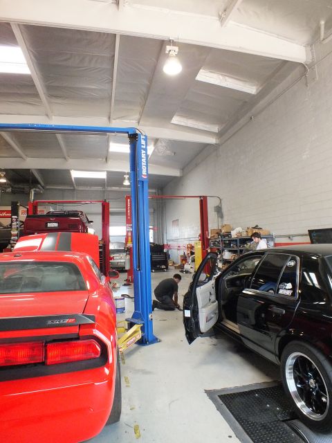 2003 Ford Crown Victoria - red Dodge Challenger and a black sedan sit inside an auto shop beside a blue two-post lift.