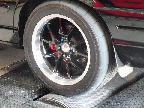2003 Ford Crown Victoria - Close-up of a black multi-spoke wheel with a Ford center cap, red brake caliper, and wide drag radial tire.