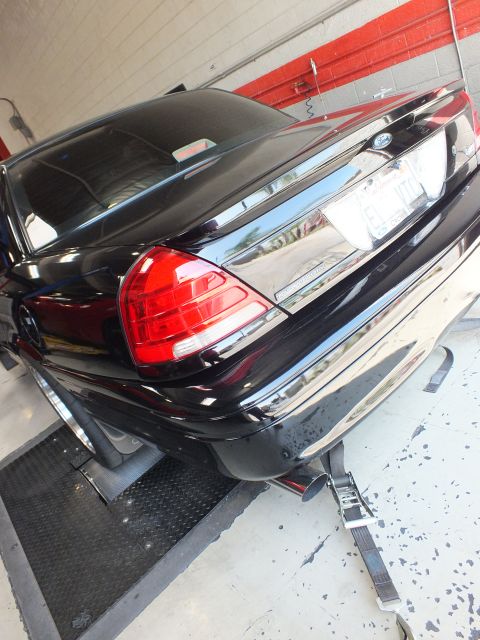 2003 Ford Crown Victoria - low rear-quarter view of a black Ford sedan shows its red taillight and trunk as it sits on shop rollers.