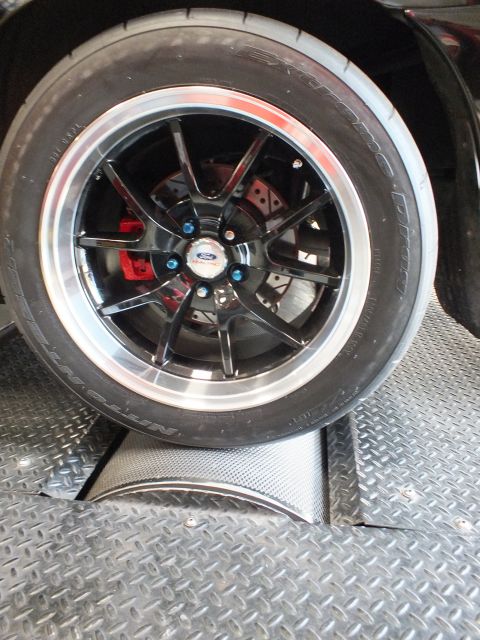 2003 Ford Crown Victoria - Close-up of a black multi-spoke Ford wheel with a red brake caliper and wide Nitto drag radial tire.