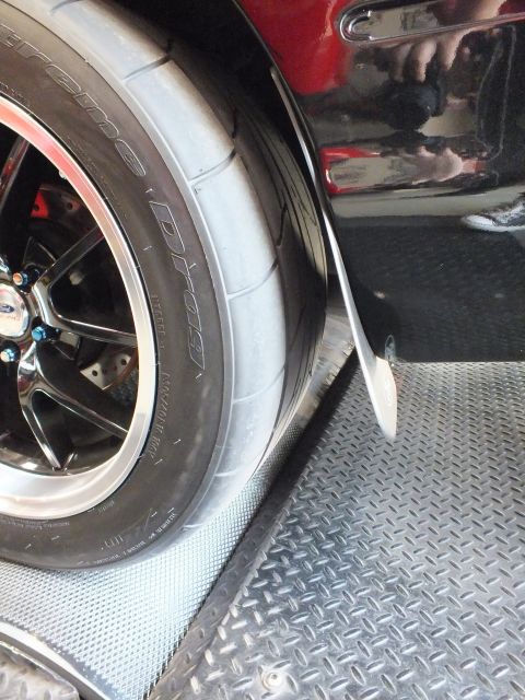 2003 Ford Crown Victoria - Close-up of a front polished wheel and wide drag radial tire on a black car parked beside a red vehicle.