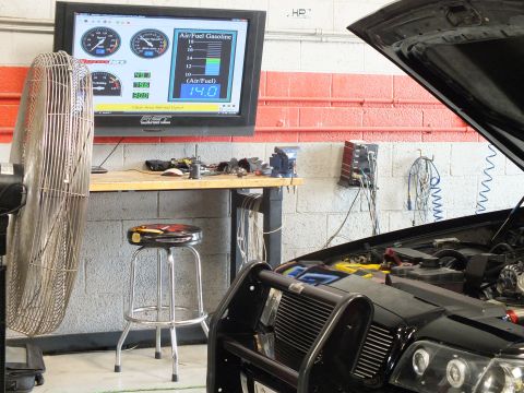 2003 Ford Crown Victoria - wall-mounted dyno monitor reads 14.0 on its air/fuel gasoline gauge above the open hood and brush guard of a black car in the garage.