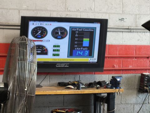 2003 Ford Crown Victoria - wall-mounted dyno monitor displays gauges with an air/fuel gasoline reading of 14.3, with a large fan in the foreground of the garage.