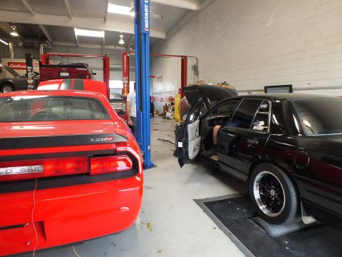2003 Ford Crown Victoria - rear of a red Dodge Challenger SRT8 fills the foreground while a black sedan sits on a dyno behind it in the shop.
