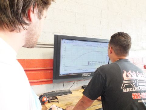 2003 Ford Crown Victoria - Two men look at a wall-mounted monitor displaying a dyno power and torque graph inside the shop.