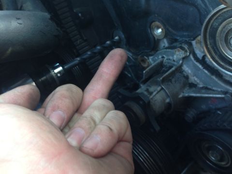 1996 Ford Probe - A drill bit is positioned near the timing belt and pulleys of an engine.