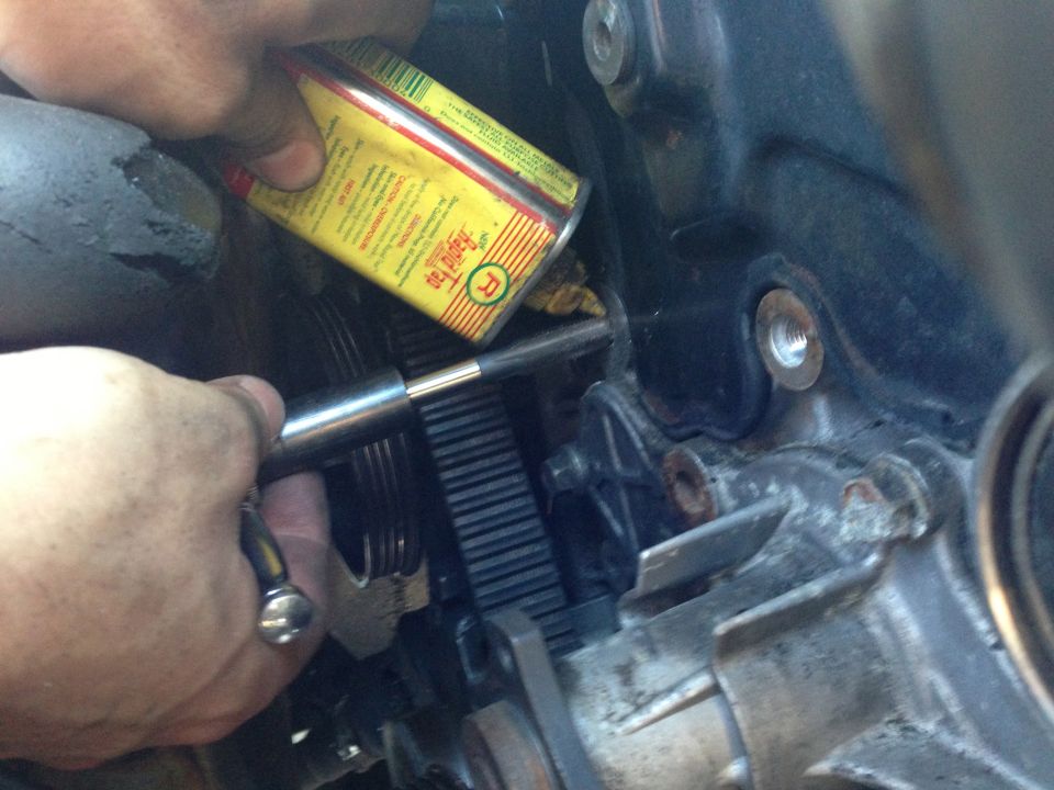 Hands working on engine timing belt with a can of oil