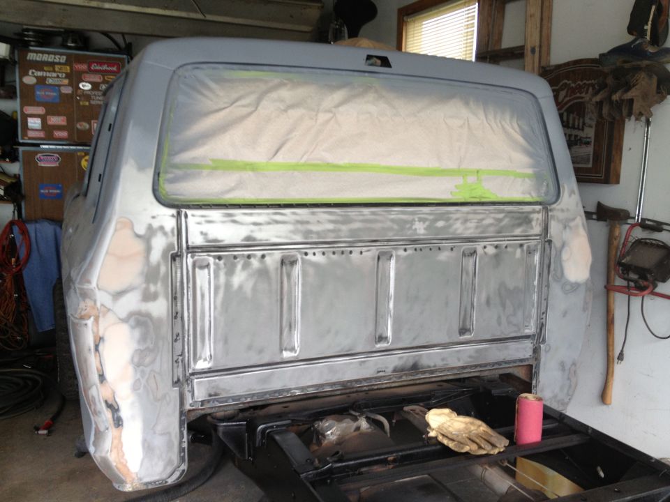 Gray truck bed and cab undergoing repair, rear view. Bodywork is exposed metal and primer